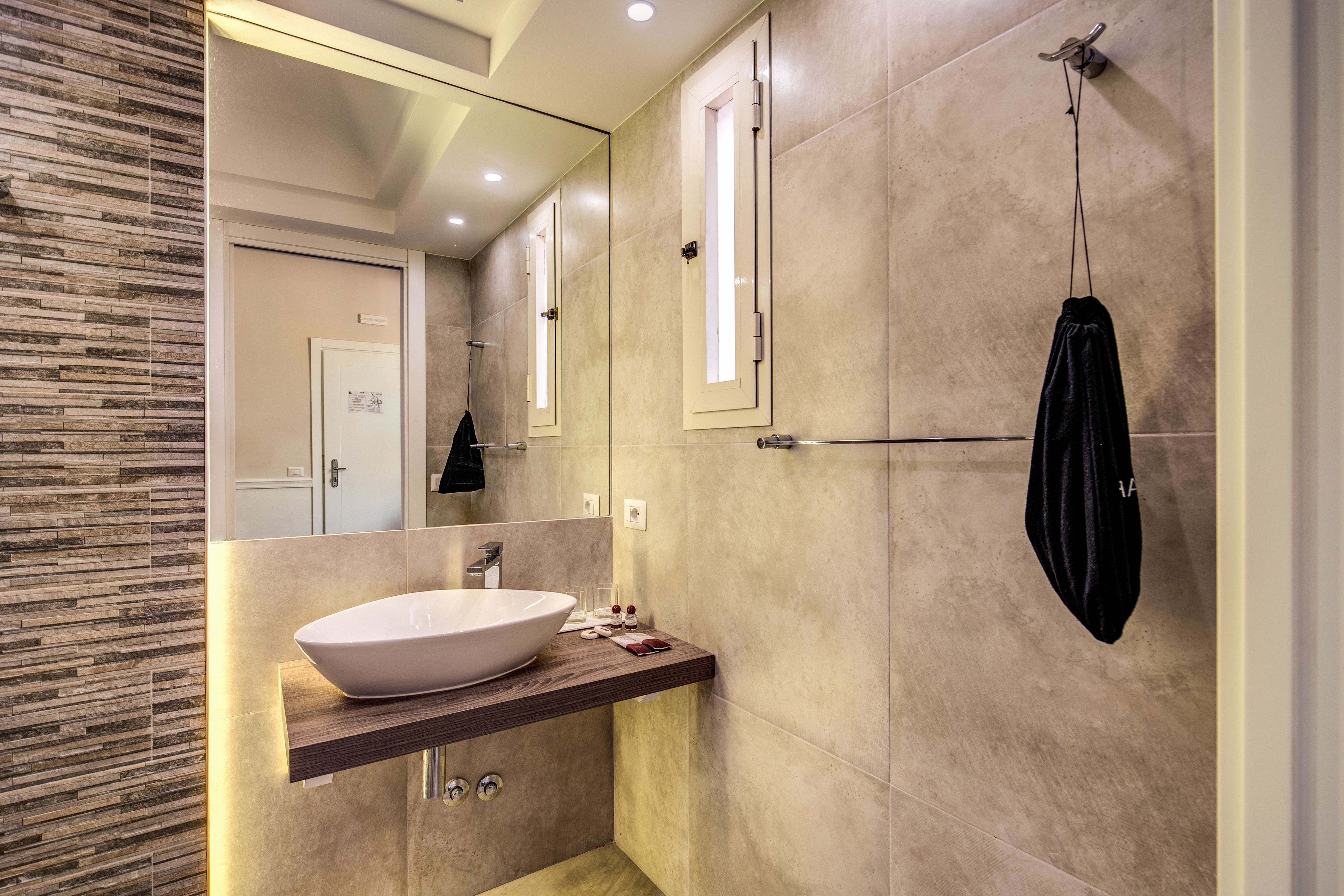 Un baño moderno con un lavamanos blanco grande, un espejo y una toalla colgada en un perchero.