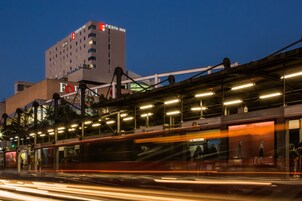 Un bâtiment moderne, avec une enseigne « Fiesta Inn » bien visible, une promenade piétonne couverte et une vue sur le paysage urbain au crépuscule.