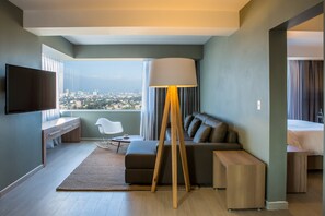 Habitación de hotel moderna con vista a la ciudad, televisor de pantalla plana, sofá, lámpara y escritorio.