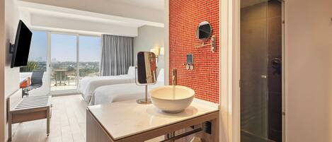 Une chambre d’hôtel avec un grand lit, une salle de bain avec un mur recouvert de carreaux rouges, un lavabo avec une grande cuve et un téléviseur fixé au mur.