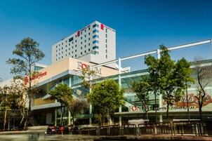 Un hôtel moderne avec une façade en verre, des espaces de détente en plein air et une enseigne « Fiesta Inn » bien visible.