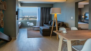 A modern hotel room with a sofa, dining table, and chairs, a TV, and a view of the city. - Fiesta Inn Express Ciudad de México Forum Buenavista (Mexico City)