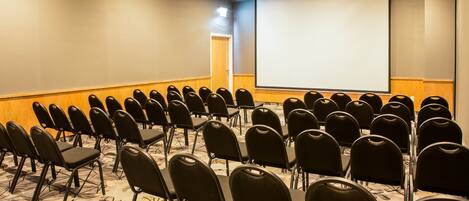 A conference room with rows of black chairs, a large screen, and a carpeted floor.