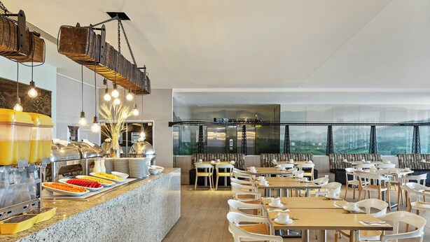A modern dining area with a buffet, seating arrangements, and a view of the city through large windows. - Fiesta Inn Express Ciudad de México Forum Buenavista (Mexico City)