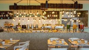 A breakfast bar with a variety of food items and beverages, white chairs, and a hanging light fixture with exposed bulbs. - Fiesta Inn Express Ciudad de México Forum Buenavista (Mexico City)