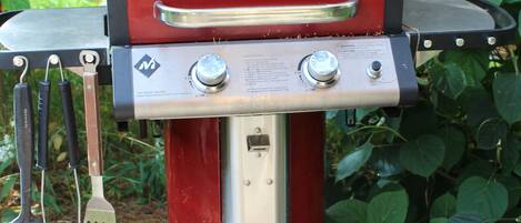 A red and silver barbecue grill with a digital display, set on a stone surface with green foliage in the background.