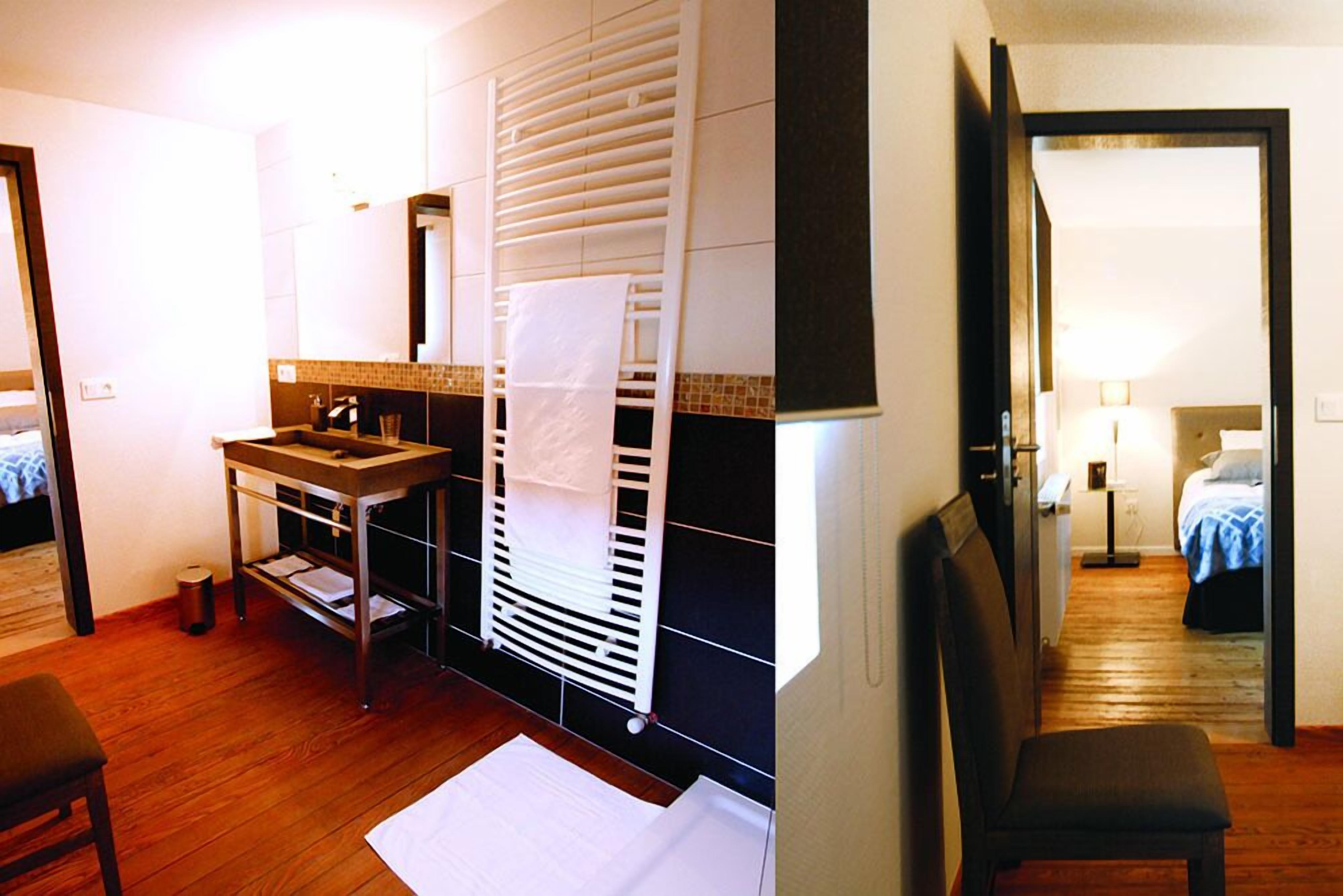 A hotel room with a wooden floor, a sink, a mirror, a radiator, and a bed with a blue blanket.