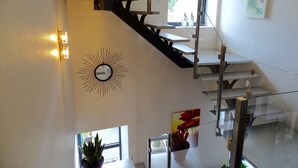 A modern staircase with glass railings, a sunburst wall clock, and a potted plant.