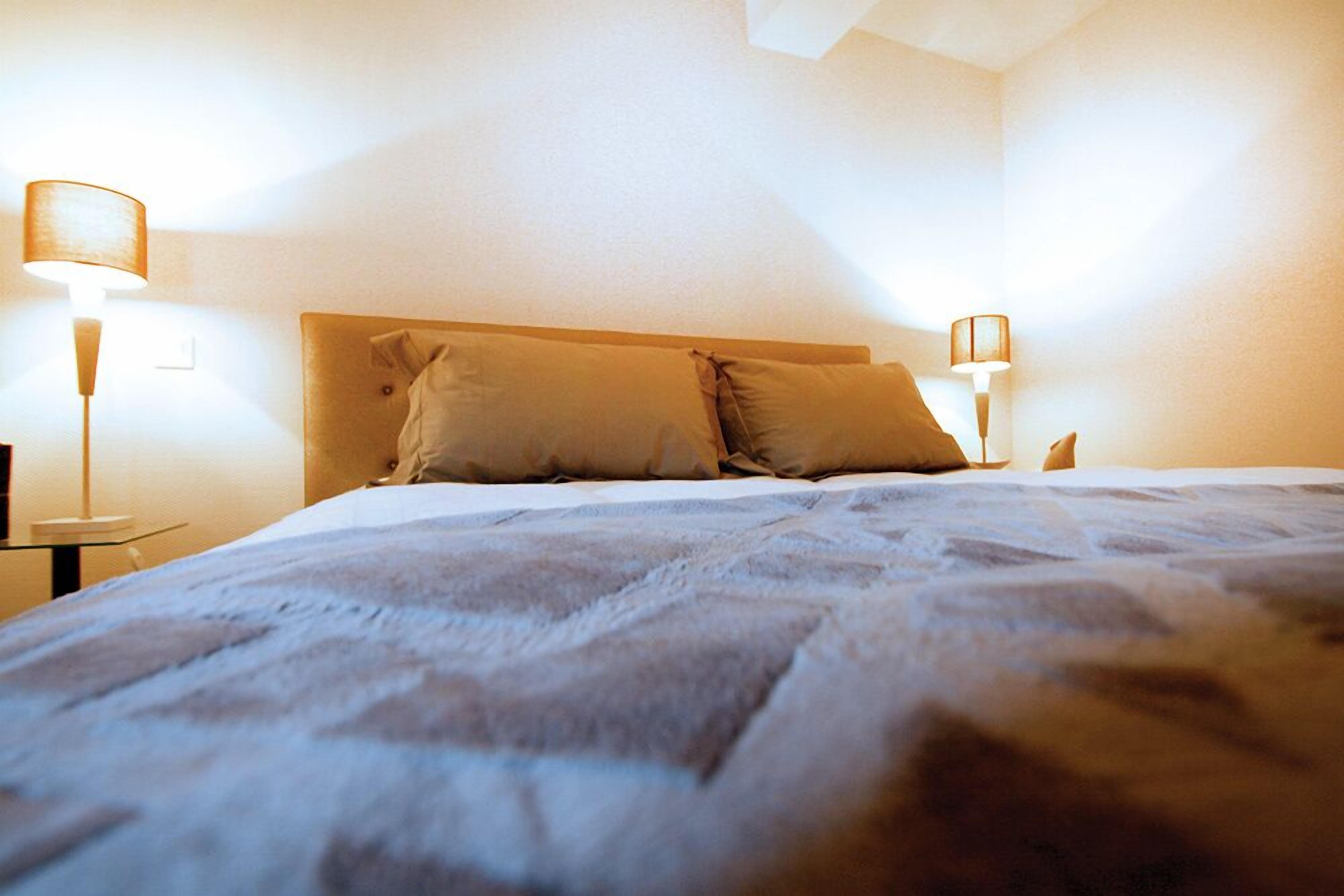 A neatly made bed with two pillows, a headboard, and two bedside lamps.
