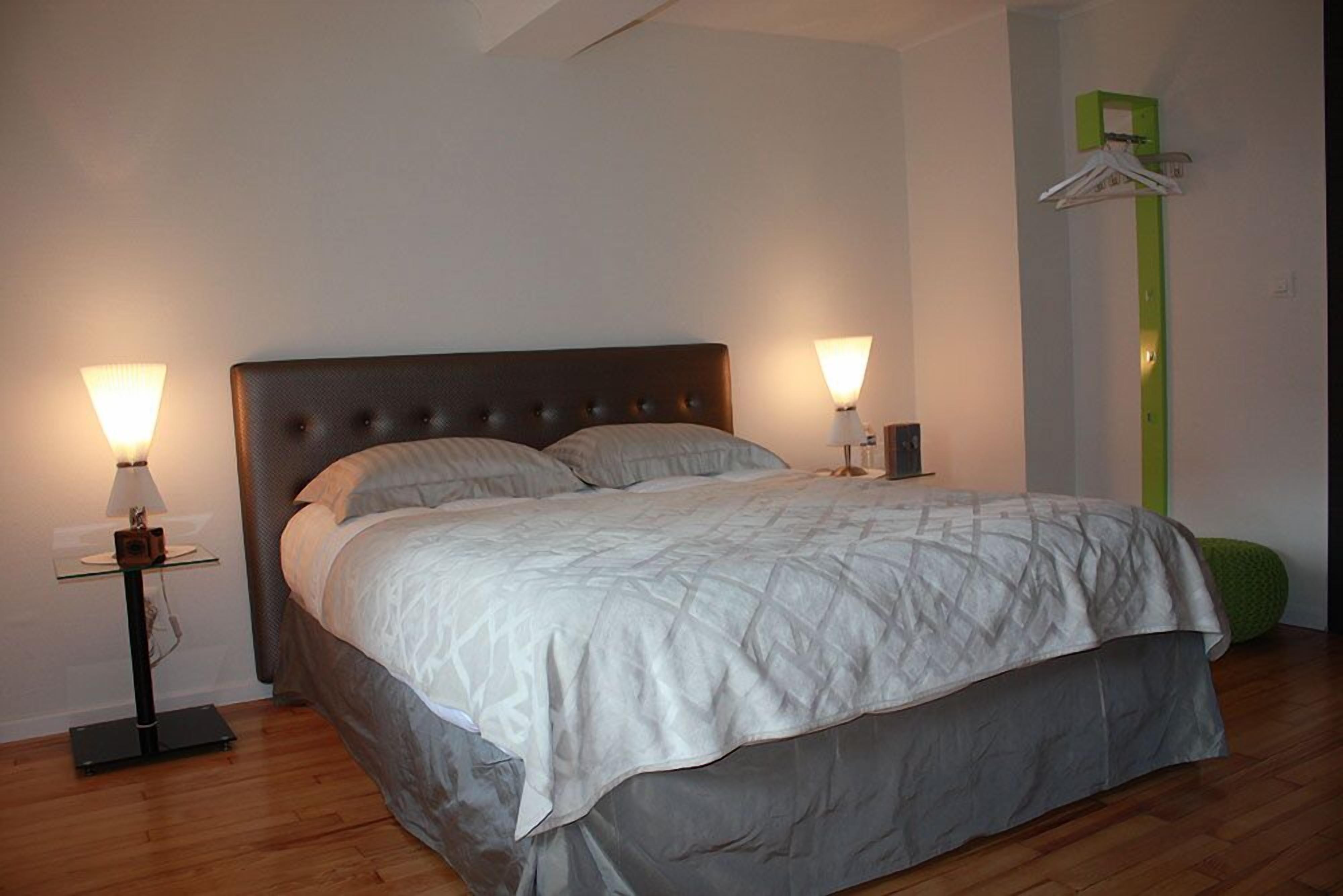 A bedroom with a bed, two bedside lamps, a green wall-mounted shelf, and a wooden floor.