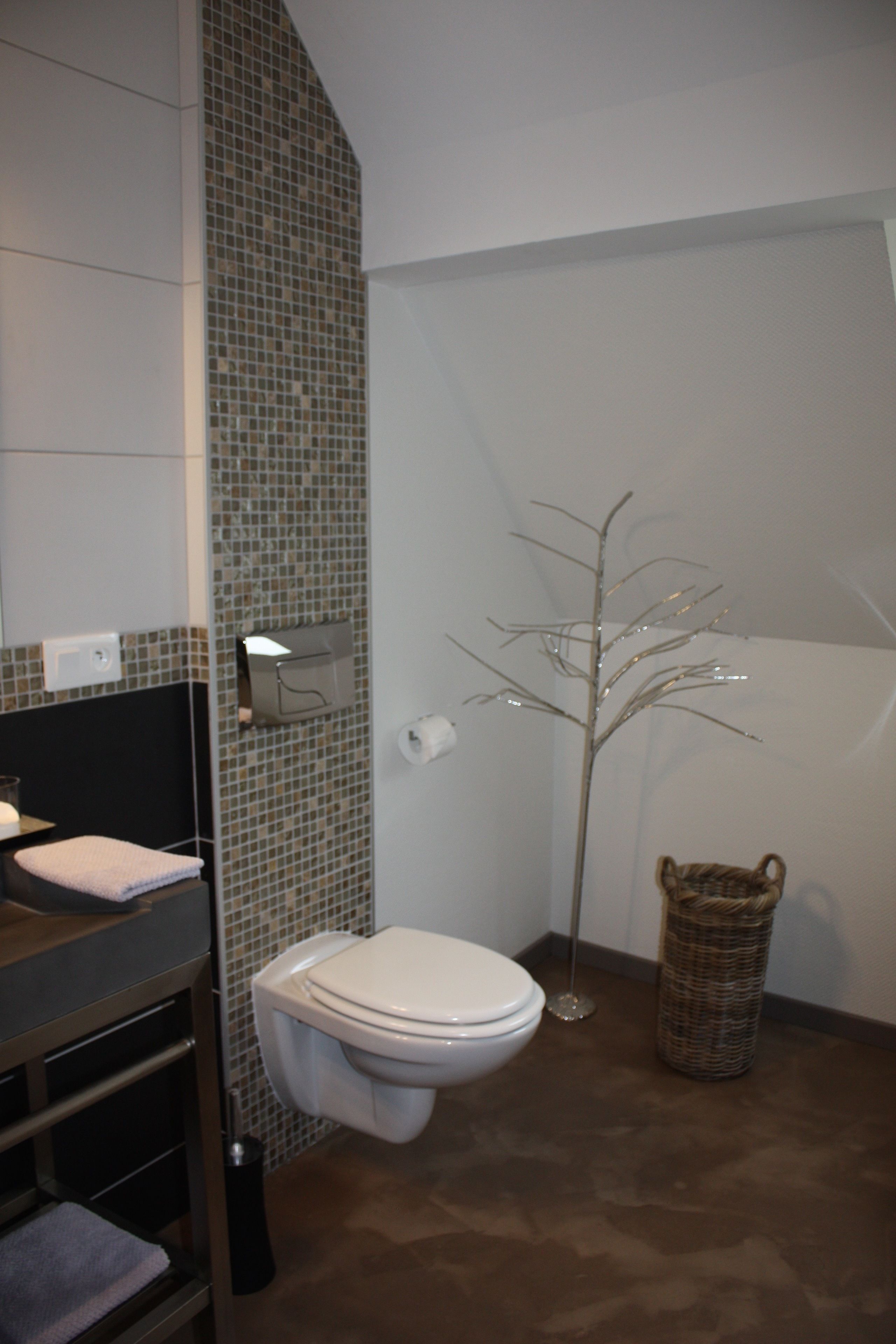 Ein Badezimmer mit Toilette, Waschbecken, Spiegel, Handtuchhalter, Mülleimer und einer Zimmerpflanze.