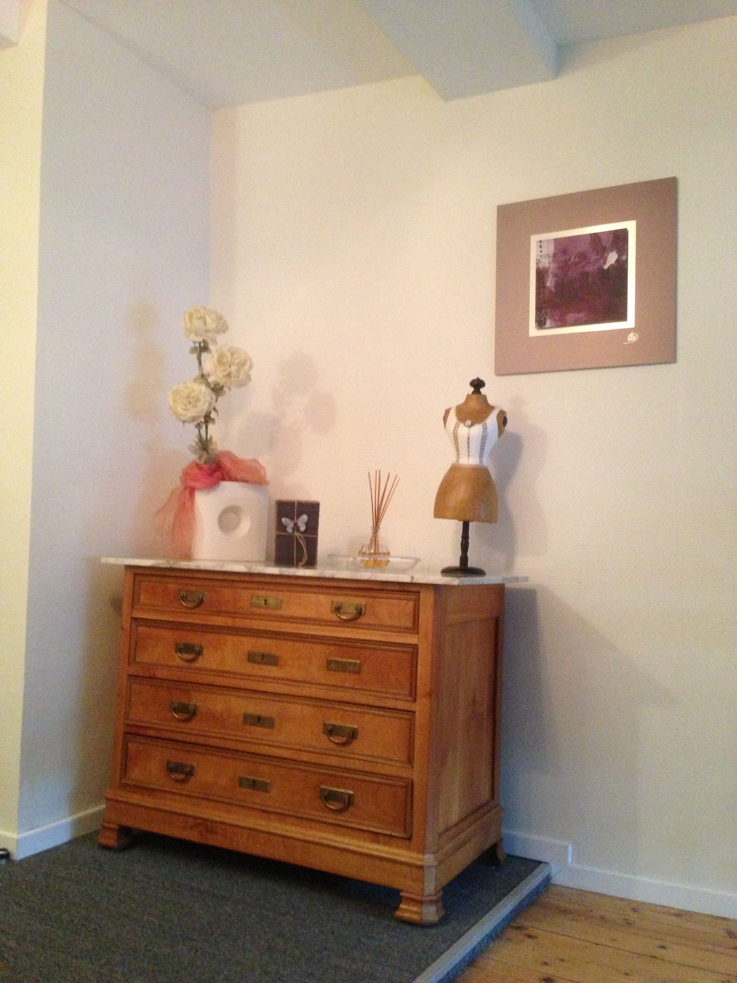A wooden dresser with drawers, a vase with flowers, a picture frame, and a lamp on top.