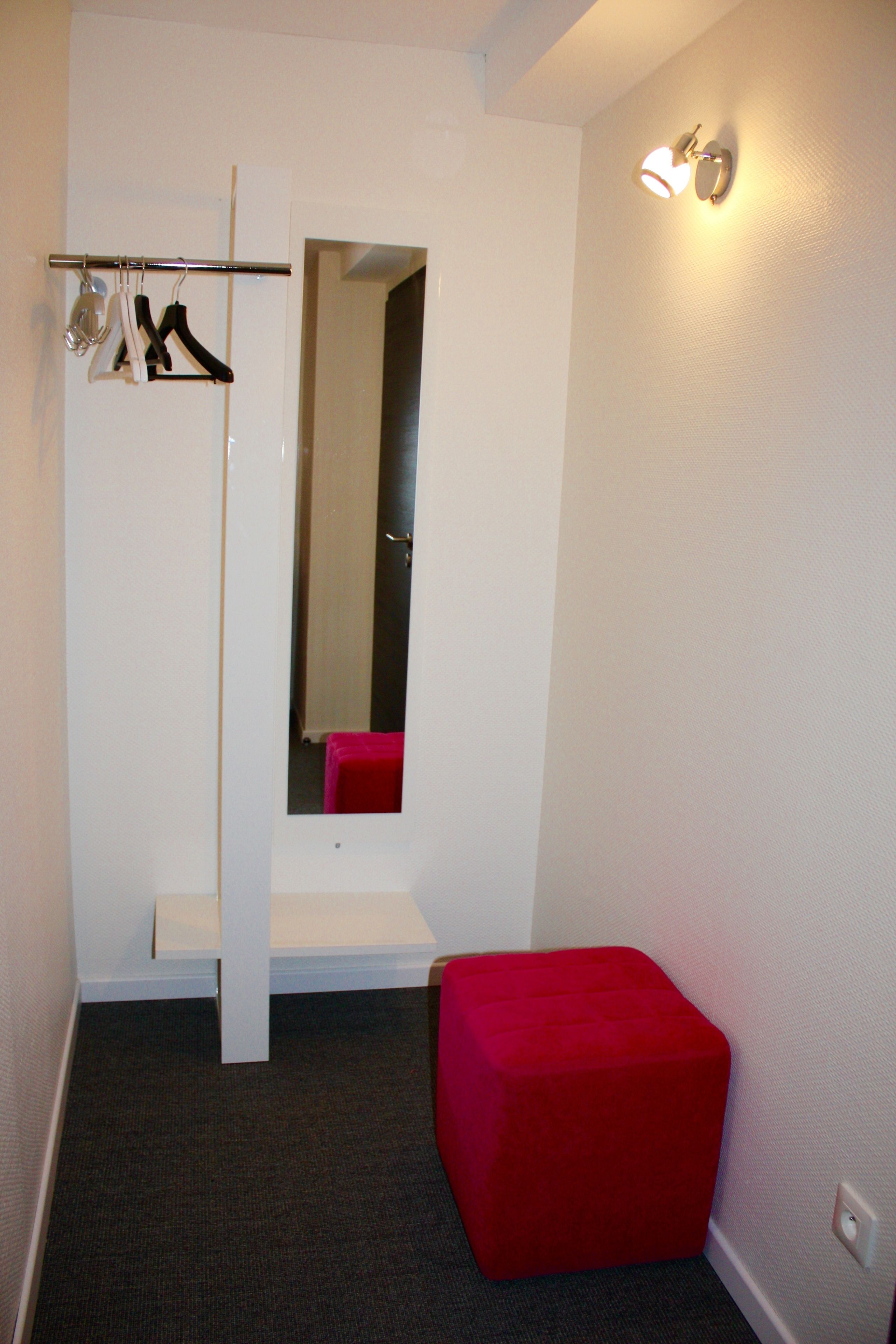 Een kleine, moderne badkamer met een witte wastafel, een rode kruk en een spiegel.