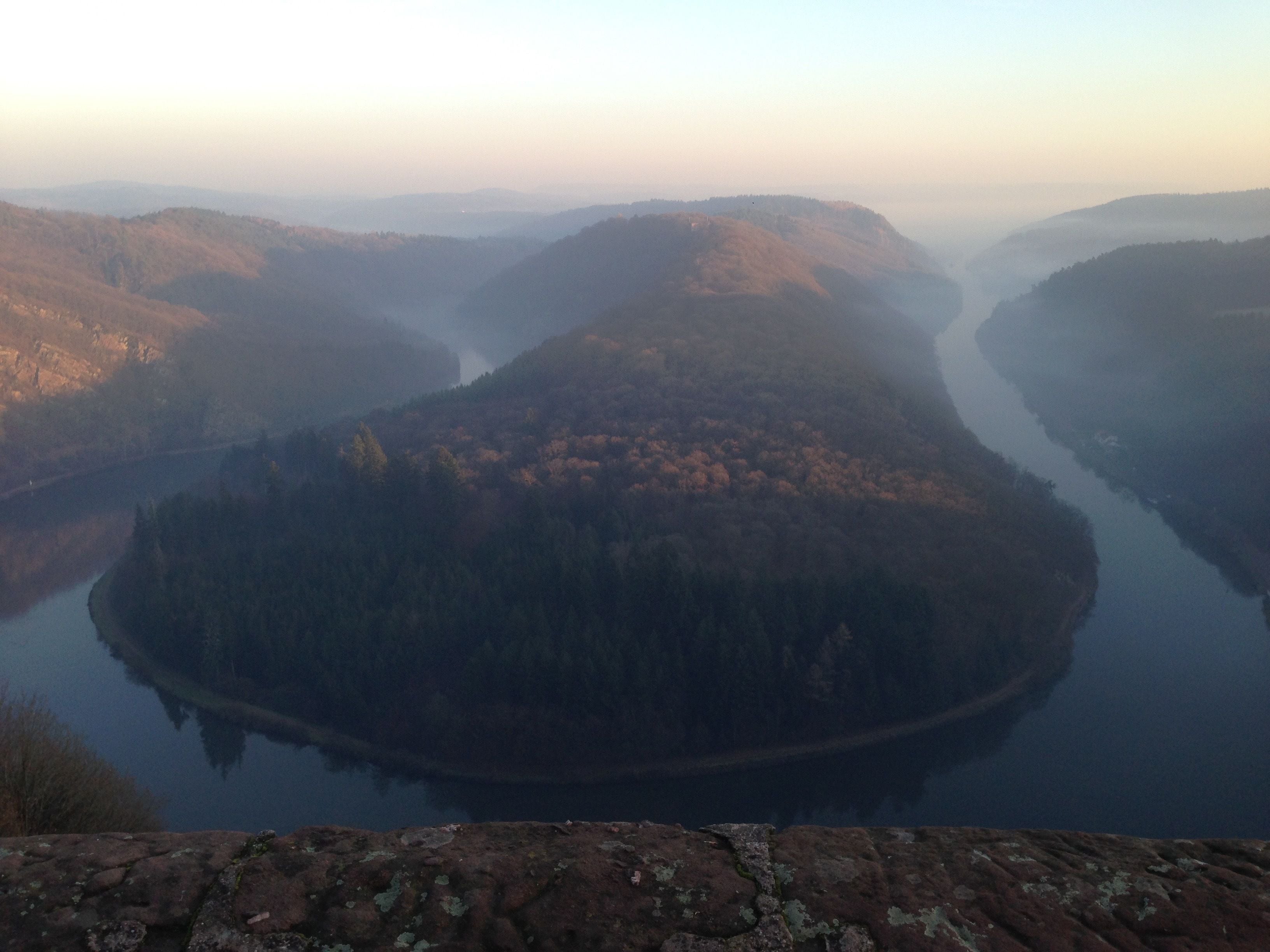 A panoramic view of a river surrounded by forested hills.