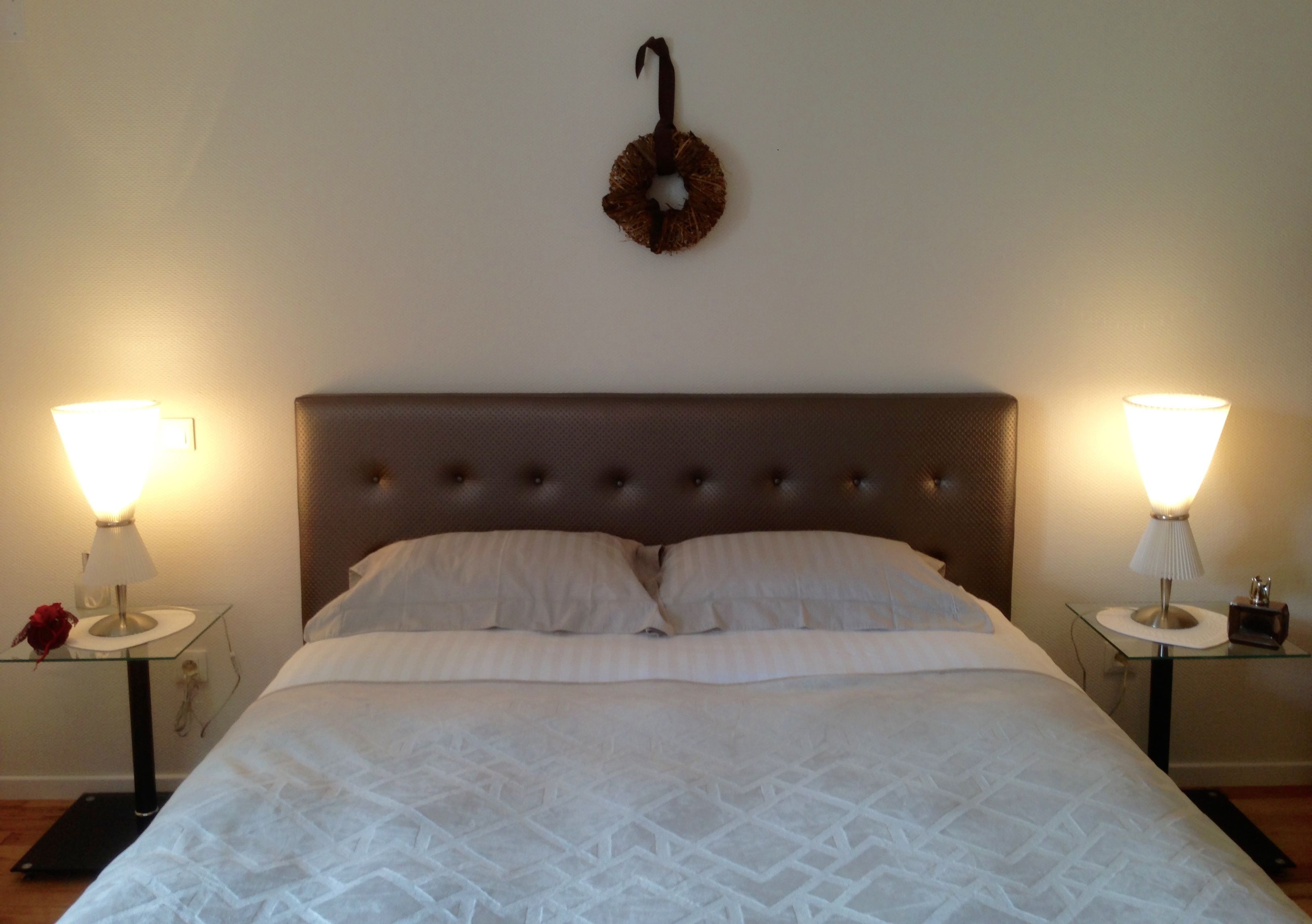A neatly made bed with a tufted headboard, two bedside tables with lamps, and a wall-mounted decoration above the bed.