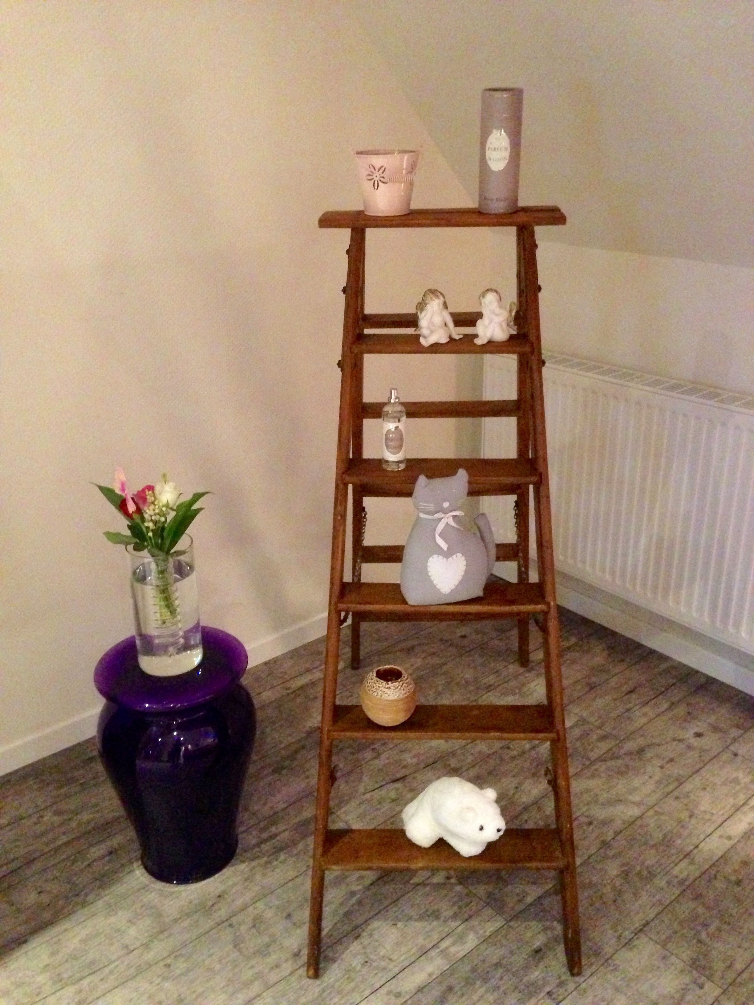 A wooden shelf with various decorative items including a vase, a candle, figurines, and a teddy bear.