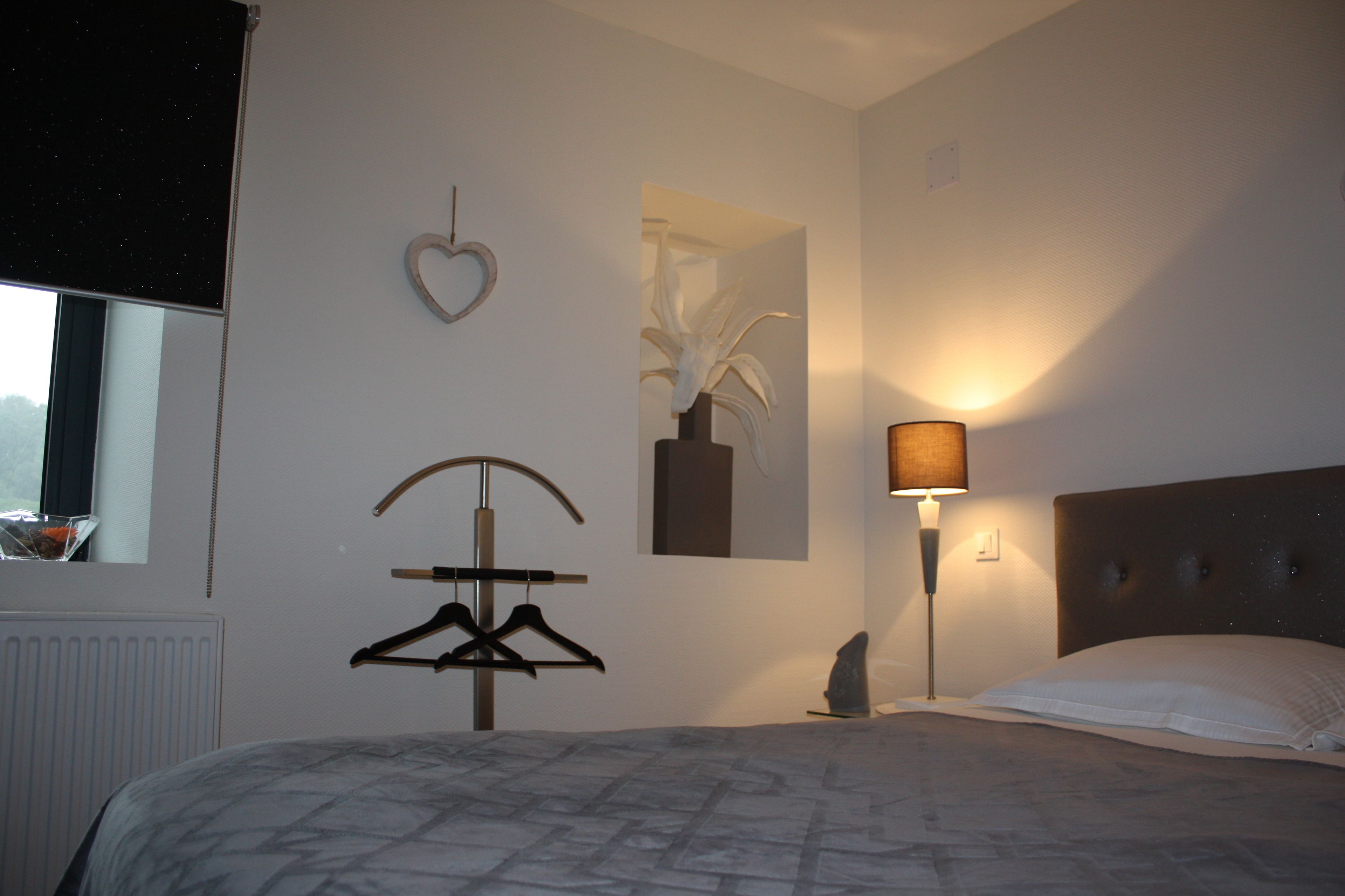 A bedroom with a bed, a hanging light, a heart-shaped decoration, and a coat rack.