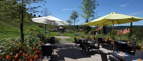 An outdoor patio with tables and chairs, surrounded by flower beds and umbrellas.