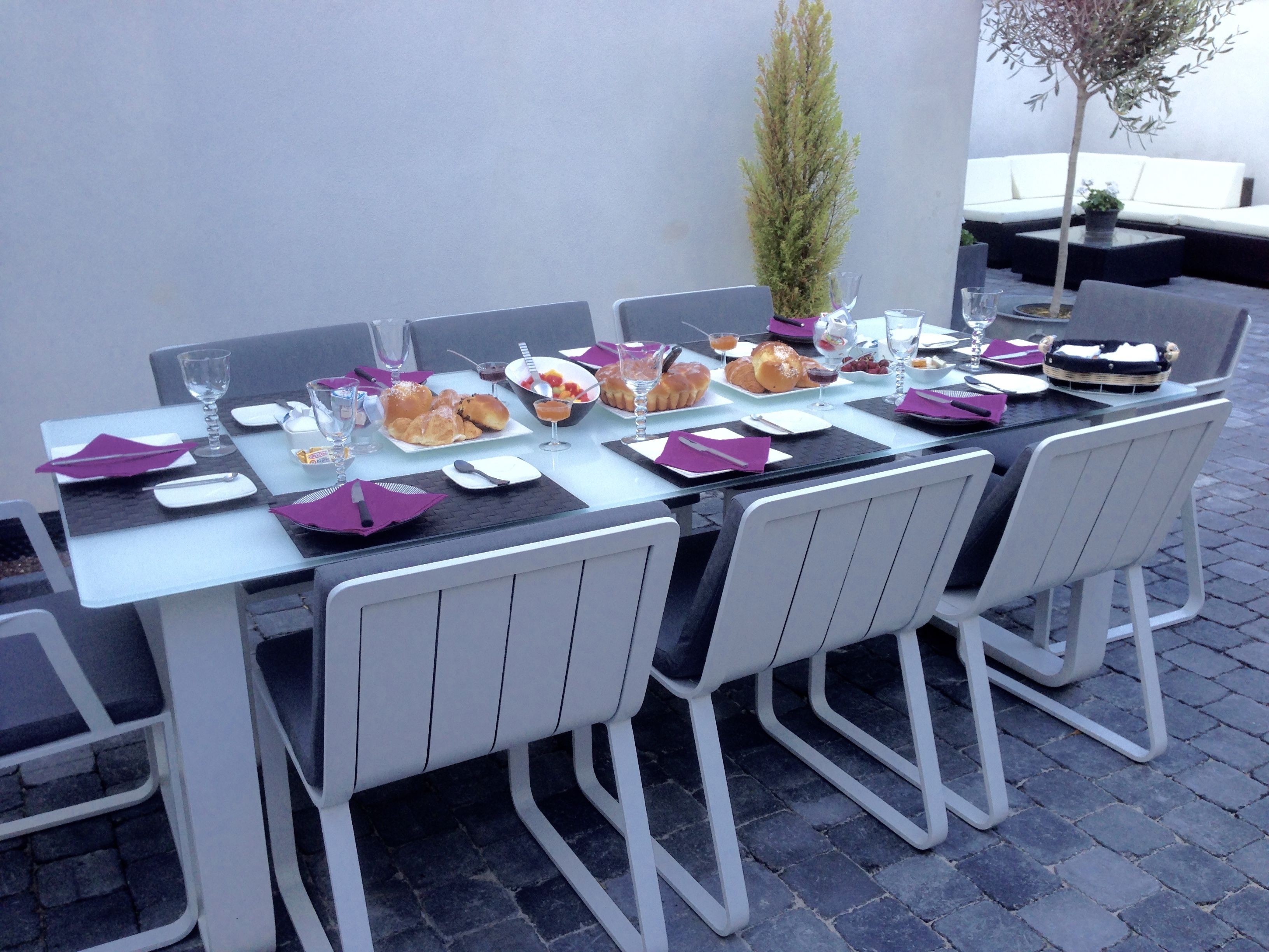 Un área de comedor al aire libre con una larga mesa dispuesta para una comida, rodeada de sillas blancas.