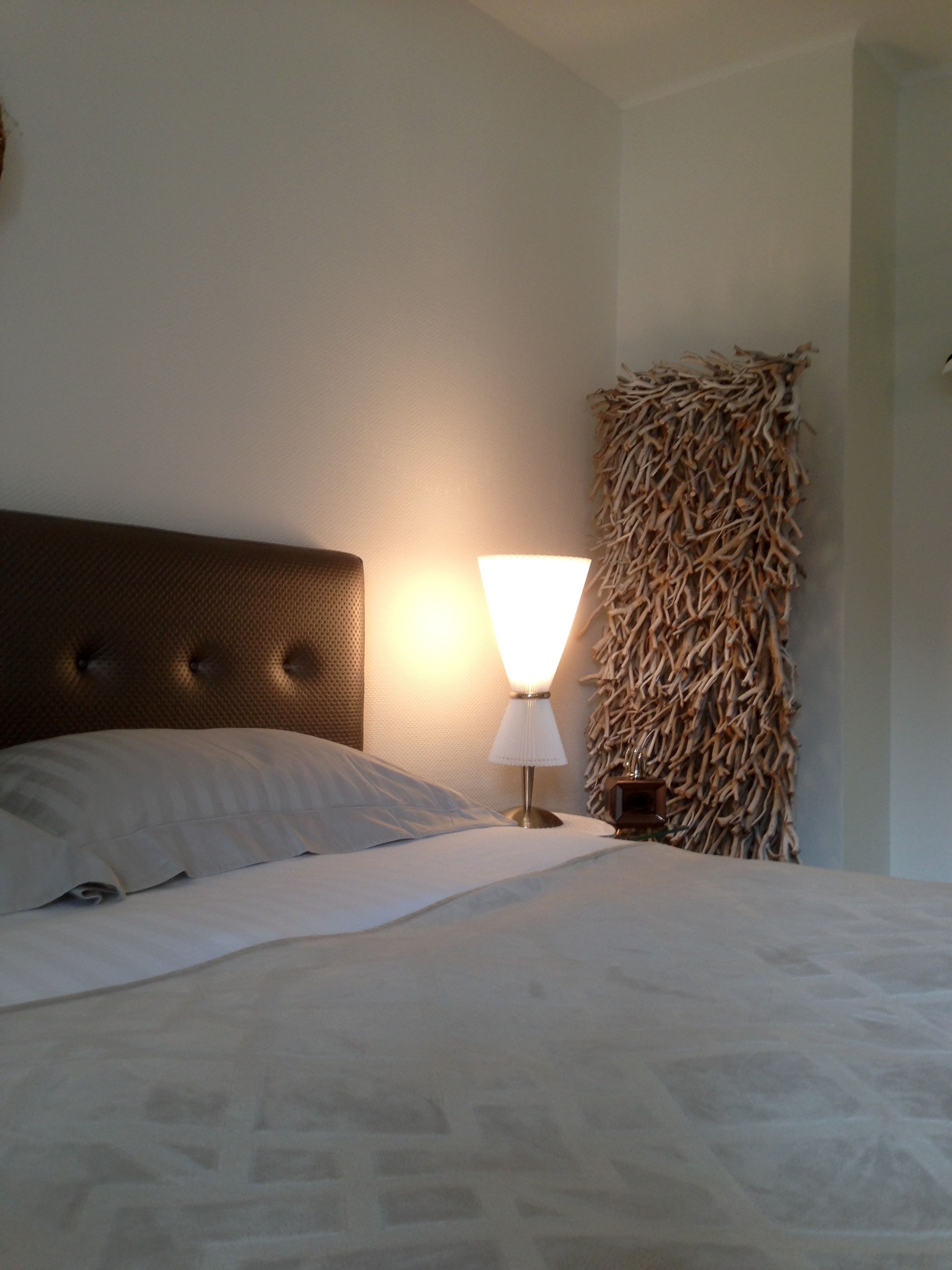 A neatly made bed with a headboard, a bedside lamp, and a wall-mounted decorative piece.