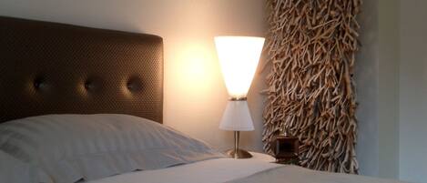 A neatly made bed with a headboard, a bedside lamp, and a wall-mounted decorative piece.