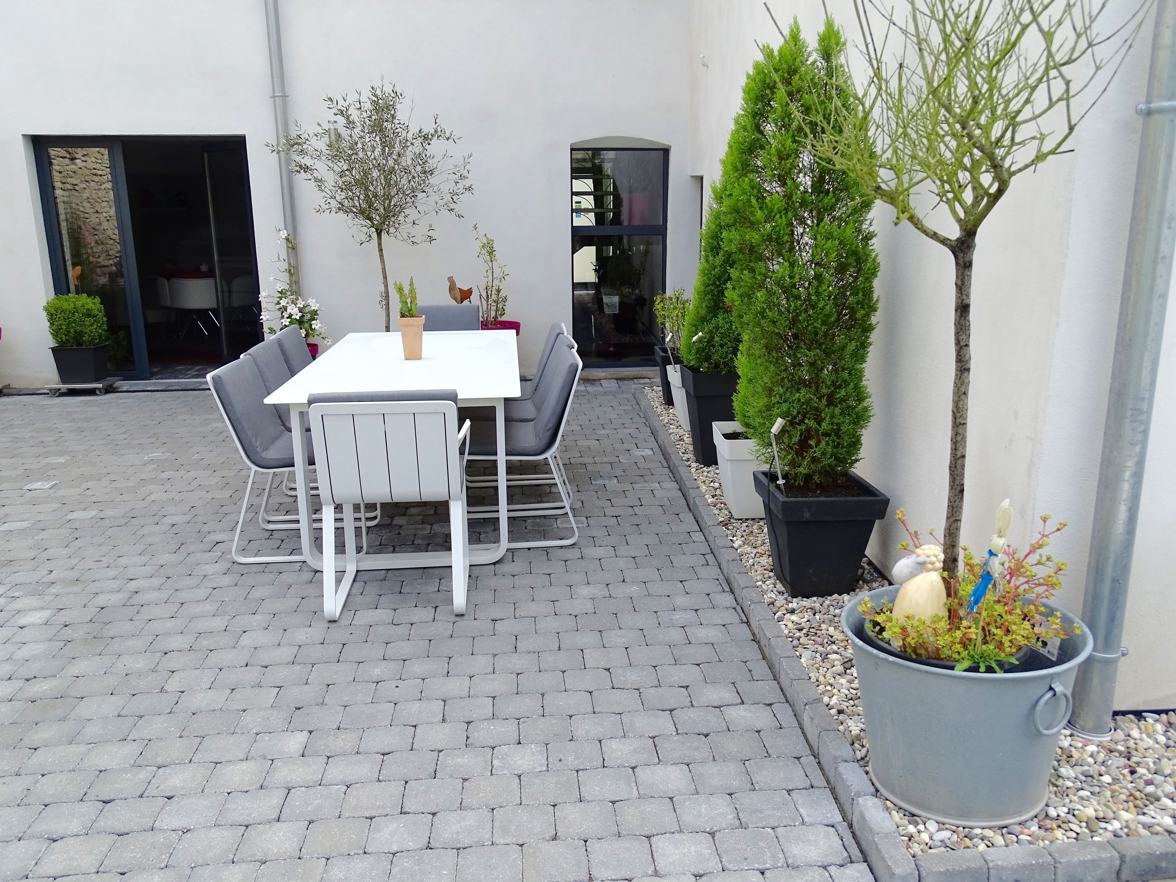 Een terras buiten met een tafel en stoelen, omringd door plantenbakken en een kleine boom.