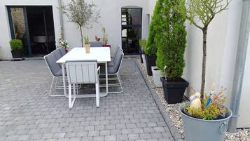 Een terras buiten met een tafel en stoelen, omringd door plantenbakken en een kleine boom.