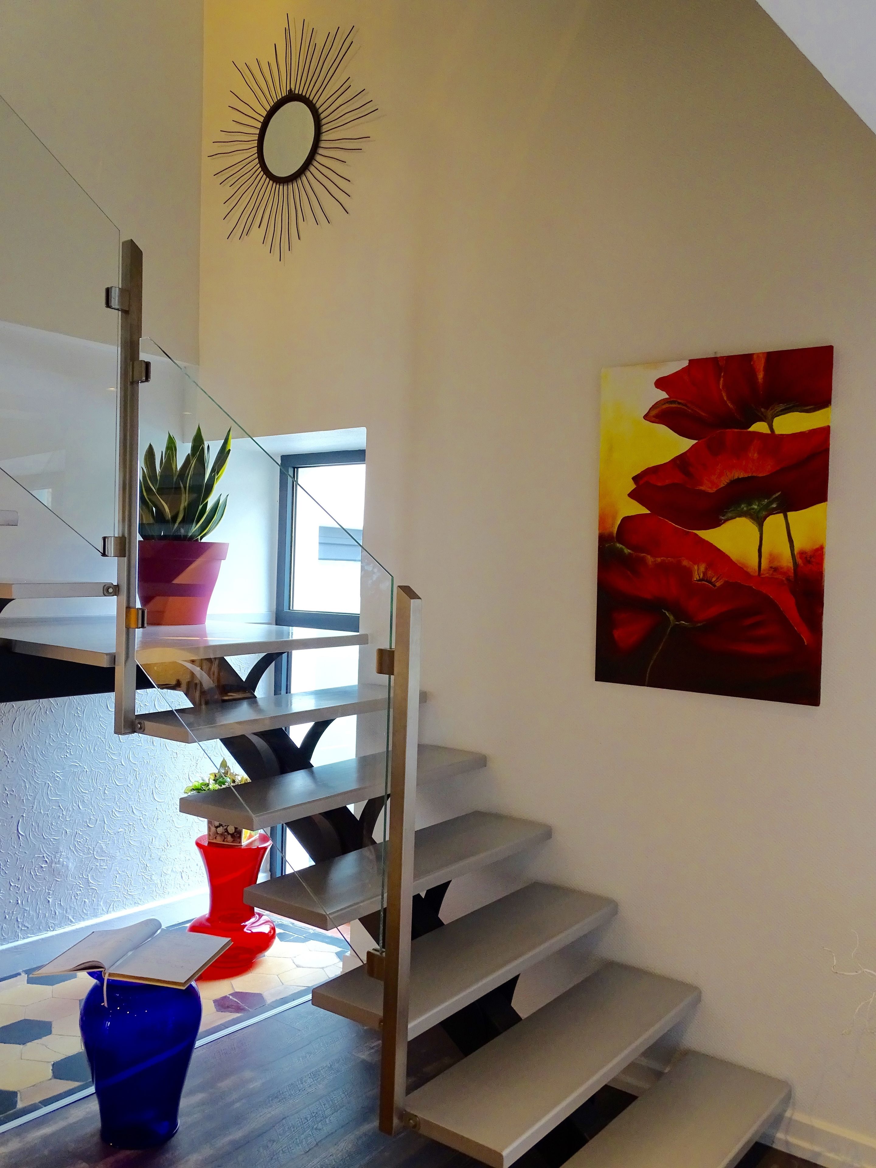 Eine Treppe mit Glastrennwand, ein Blumentopf und ein Gemälde mit roten Blumen an der Wand.