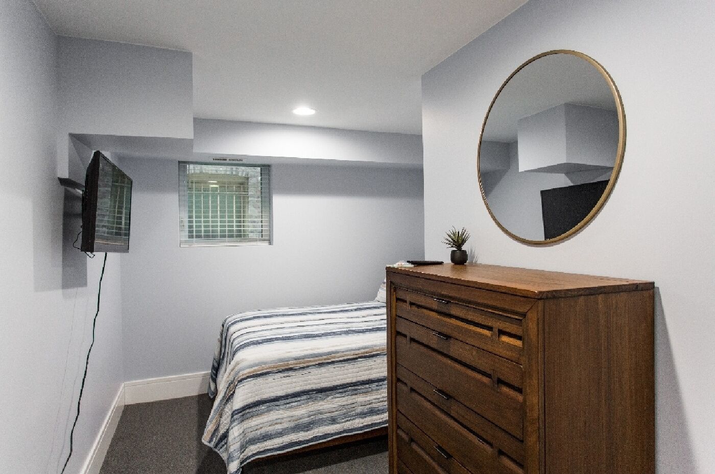 A bedroom with a bed, a dresser, a mirror, a window, and a TV.