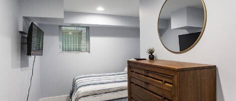 A bedroom with a bed, a dresser, a mirror, a window, and a TV.