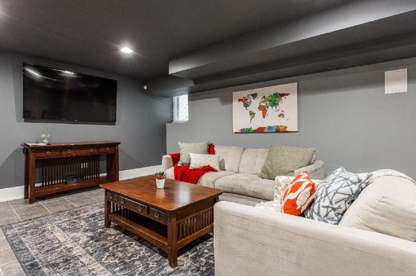Un salon avec un mur de couleur gris foncé, un grand téléviseur à écran plat, une œuvre d’art représentant une carte du monde, un canapé beige et une table basse en bois.
