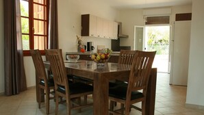 A dining area with a wooden table and chairs, a fruit bowl, and a kitchen in the background. - House / Villa - Port-Vecchio (Porto-Vecchio)