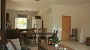A living room with a leather sofa, wooden dining table, and chairs. There is a kitchen area with a refrigerator and a dining table. - House / Villa - Port-Vecchio (Porto-Vecchio)