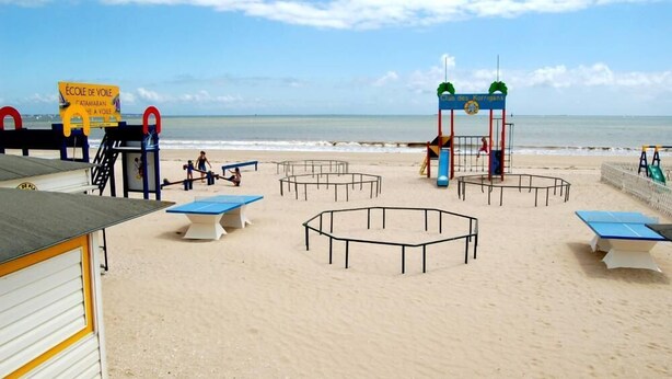 Een strand speeltuin met tafels en speeltoestellen, waaronder een klimrek en een glijbaan.