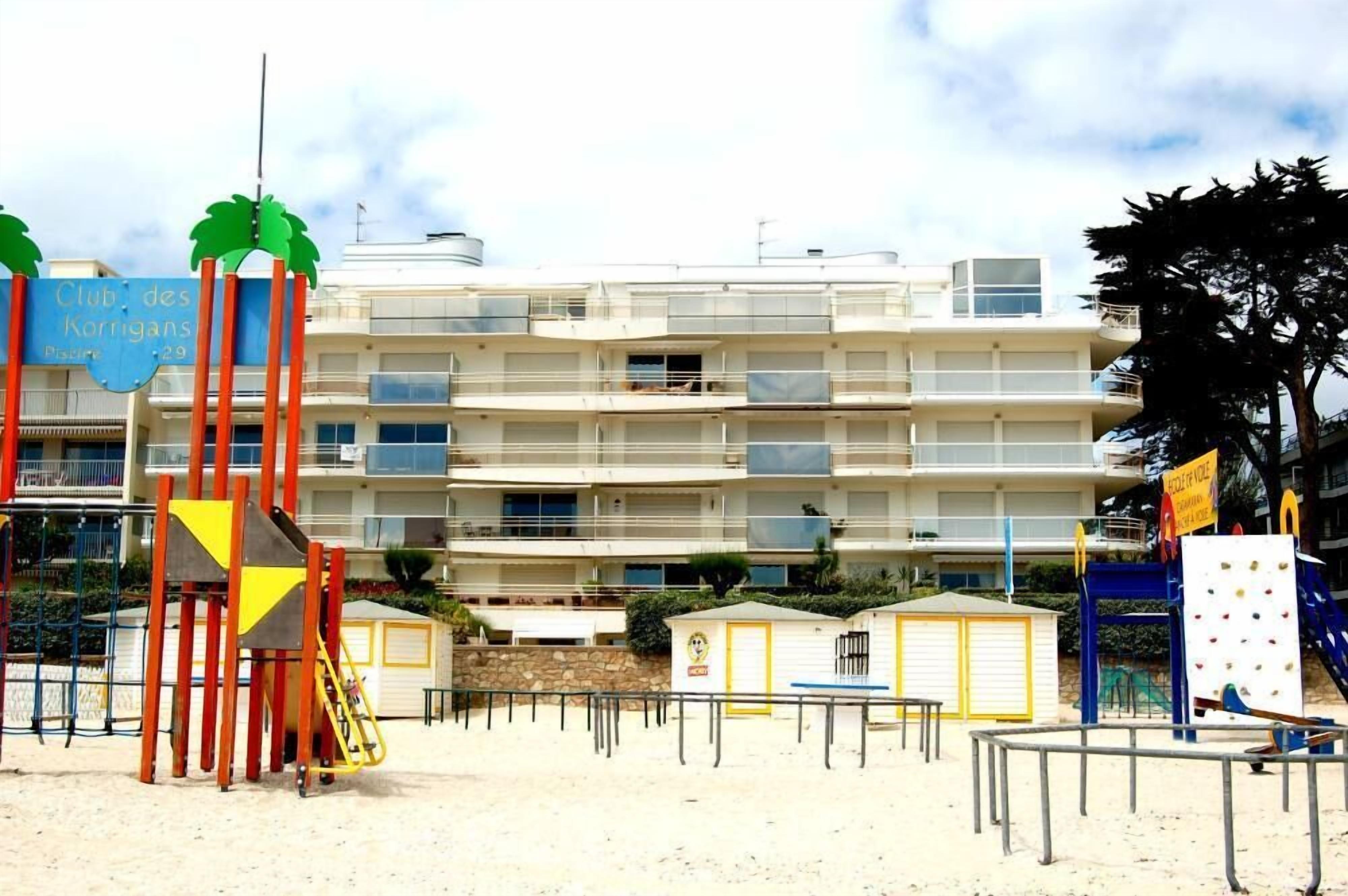 A beachfront hotel with multiple balconies, a playground, and a beach area.
