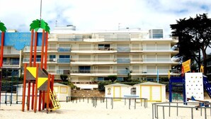 Een hotel aan het strand met meerdere balkons, een speelplaats en een strandgedeelte.