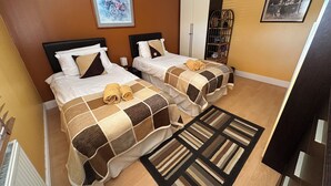 A hotel room with two beds, a wardrobe, a bookshelf, and a framed picture on the wall. - Excellent ground floor 2 Bed apt overlooking golf course with private parking. (Watton)