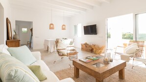 Un salon lumineux avec un canapé blanc, une table basse en bois, des fauteuils en osier et un téléviseur à écran plat.