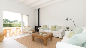 Un salon moderne avec un canapé blanc, une table basse en bois et une vue sur un jardin grâce à de grandes fenêtres.