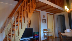 A wooden staircase leading to a loft area with a television and storage crates.