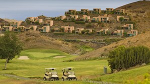 A golf course with a desert landscape and modern buildings in the background. - Salobre Golf Lagos 40 by VillaGranCanaria (San Bartolomé de Tirajana)
