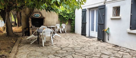A stone-paved courtyard with outdoor seating, a stone fireplace, and a white building with shutters.
