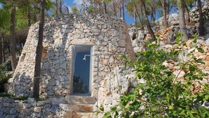 A stone-built outdoor shower with a metal door, surrounded by trees and rocky terrain. - Luxury Villa & Spa (Gagliano del Capo)