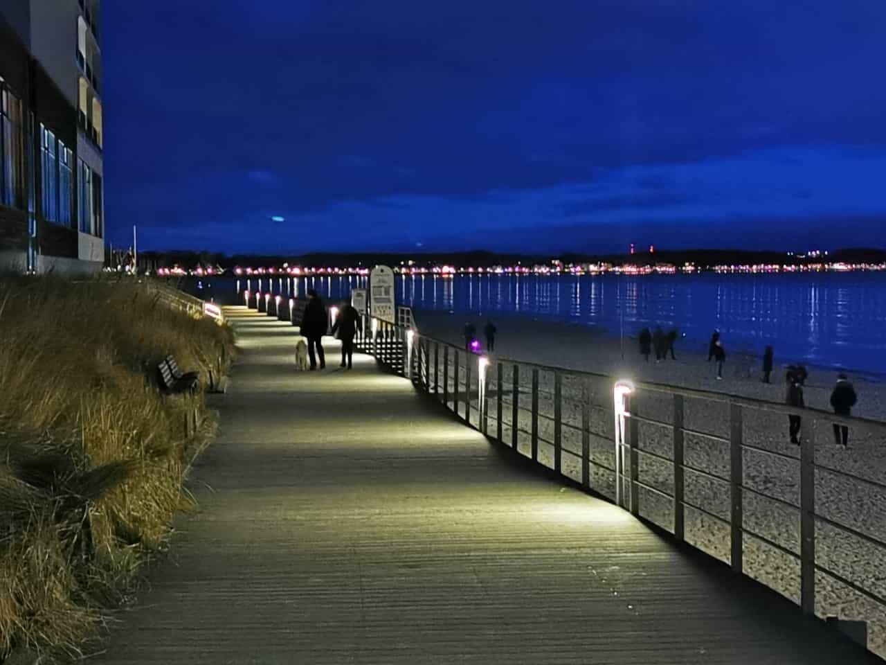 A wooden boardwalk leading to a beach with a railing on one side and a building on the other.