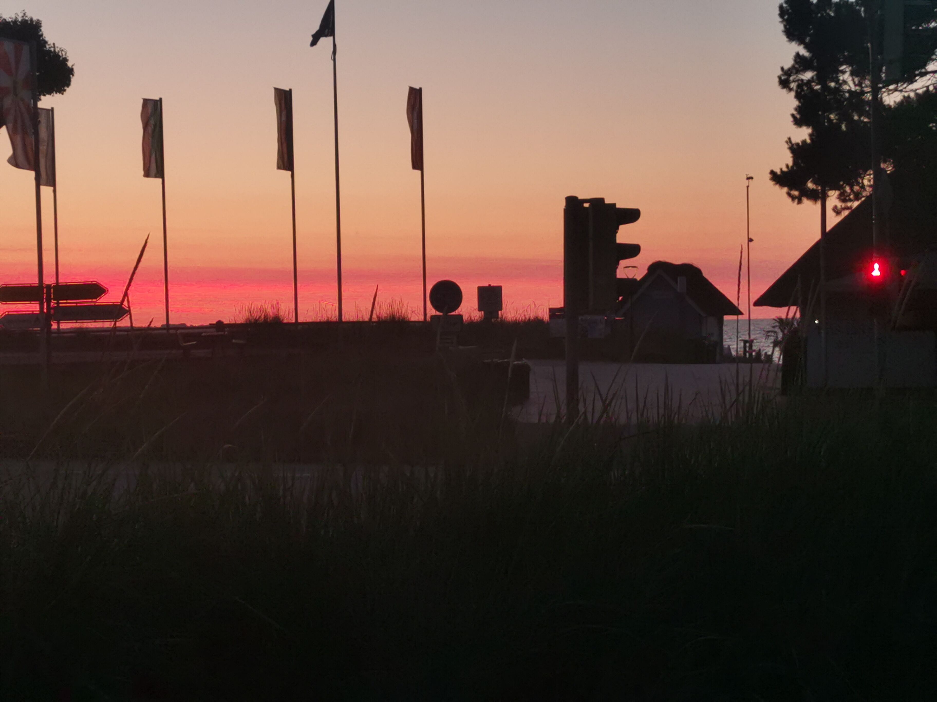 A sunset with silhouettes of flags, a traffic light, and a building.