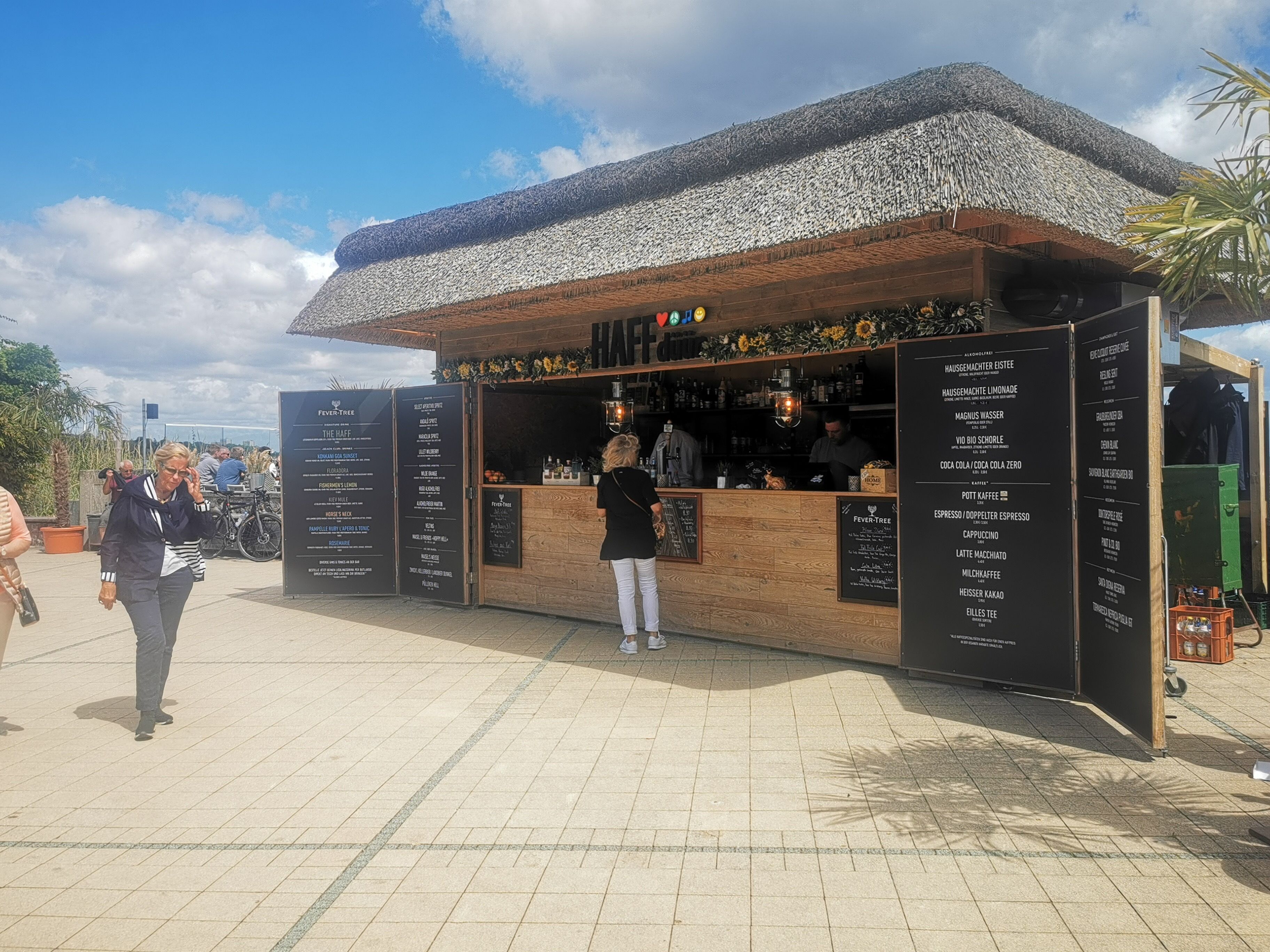 A food kiosk with a thatched roof, a menu board, and a bar area.