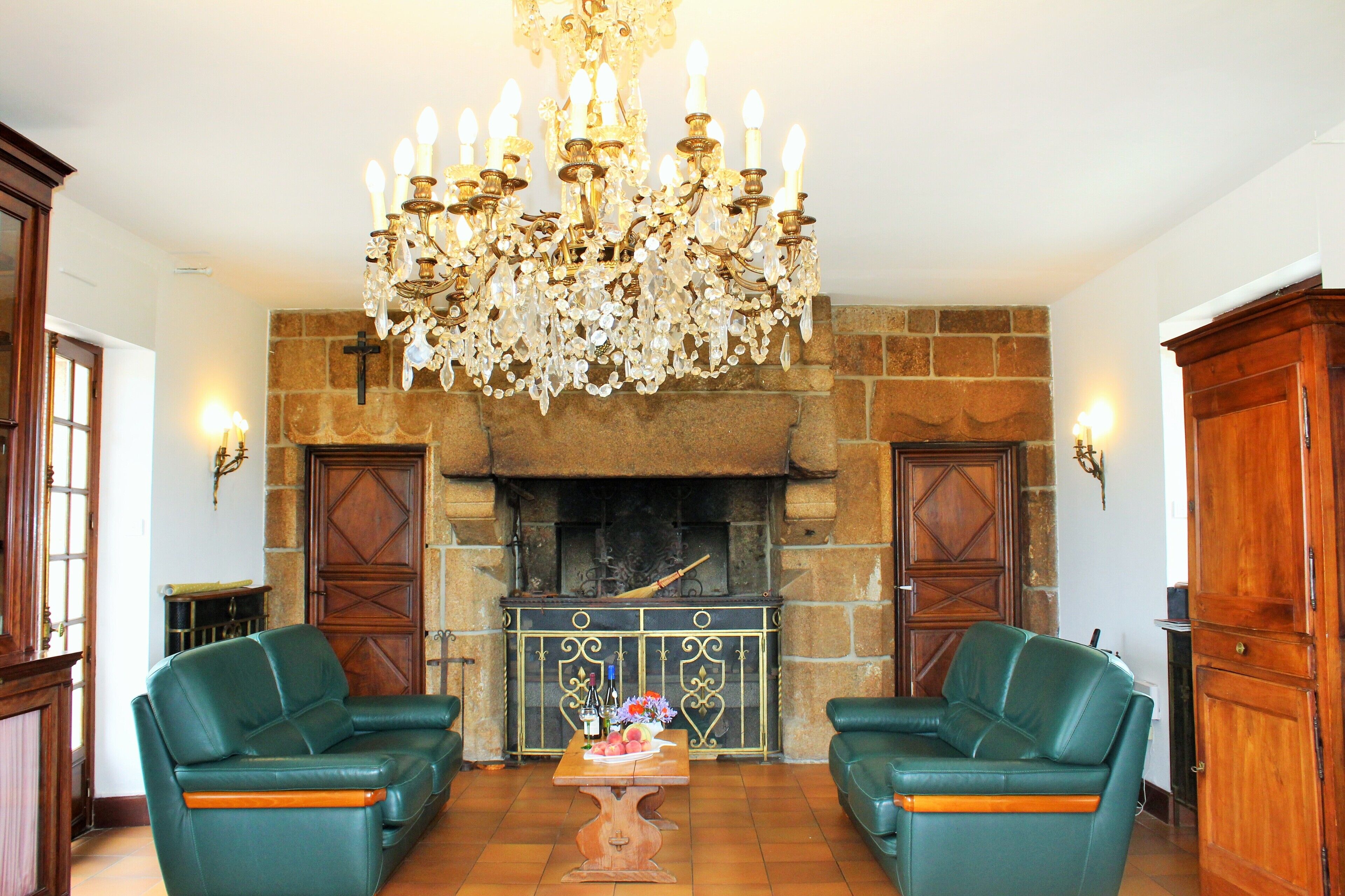 Ein Zimmer mit Kamin, zwei grünen Ledersofas, einem Holztisch mit einer Vase und einer großen Chandelier.