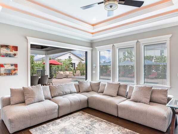 A modern living room with a sectional sofa, a ceiling fan, and large windows. - Luxury Resort Lakefront Pool Spa Villa (Thonotosassa)