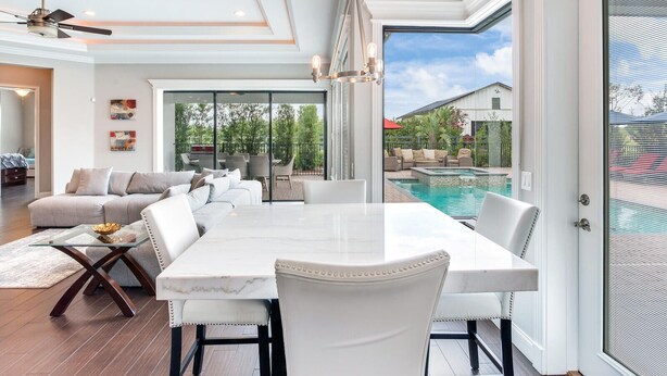 A spacious living area with a large dining table, comfortable seating, and a view of a swimming pool.