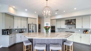 A modern kitchen with a large island, white cabinetry, stainless steel appliances, and a chandelier.